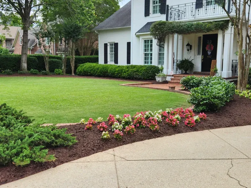White house with green lawn and flower bed along a driveway.