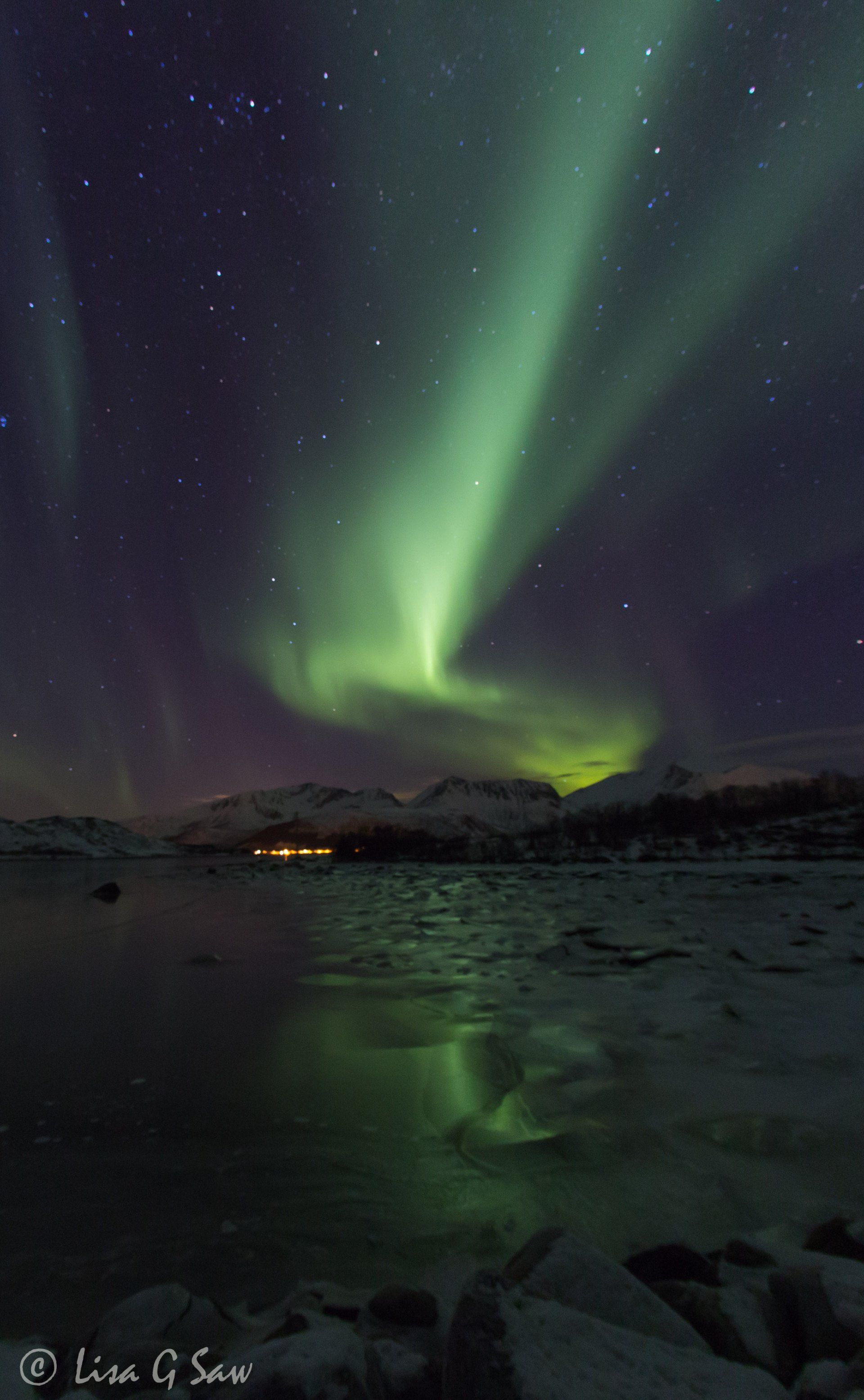 Northern Lights reflecting on ice and with town lights, Norway