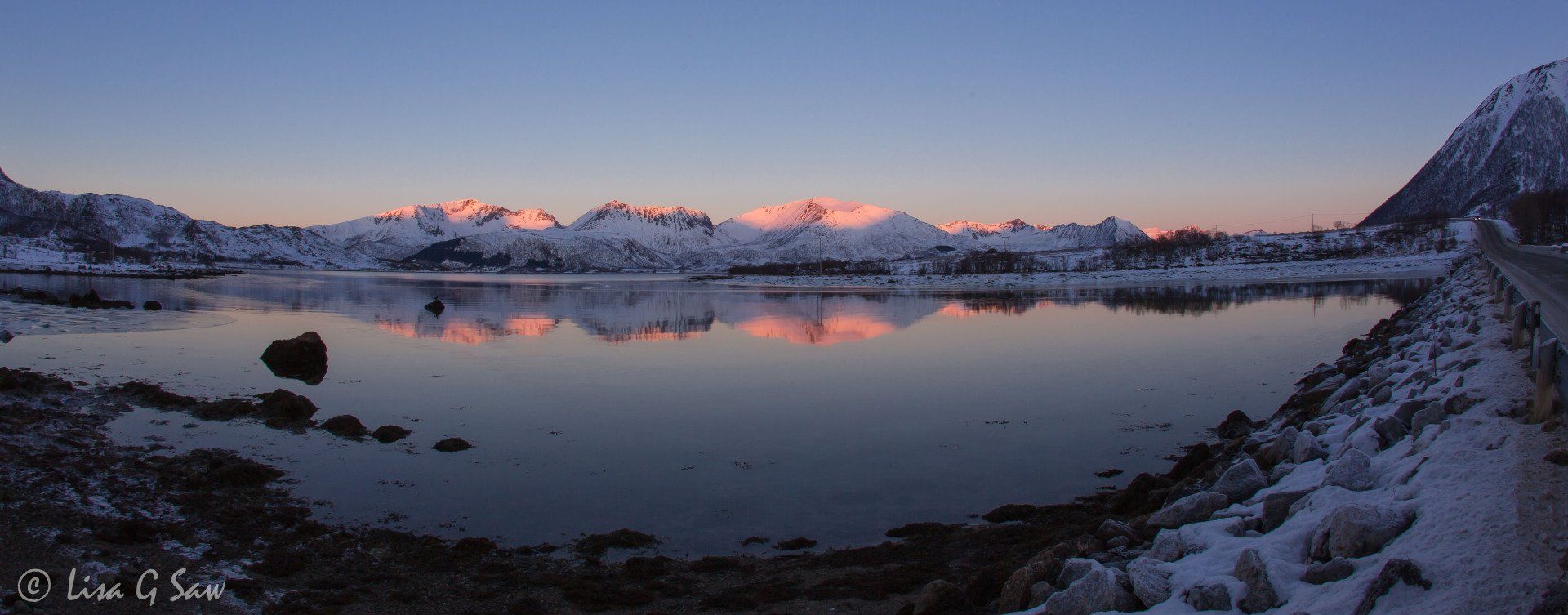 Snow covered mountains reflected in water at sunrise