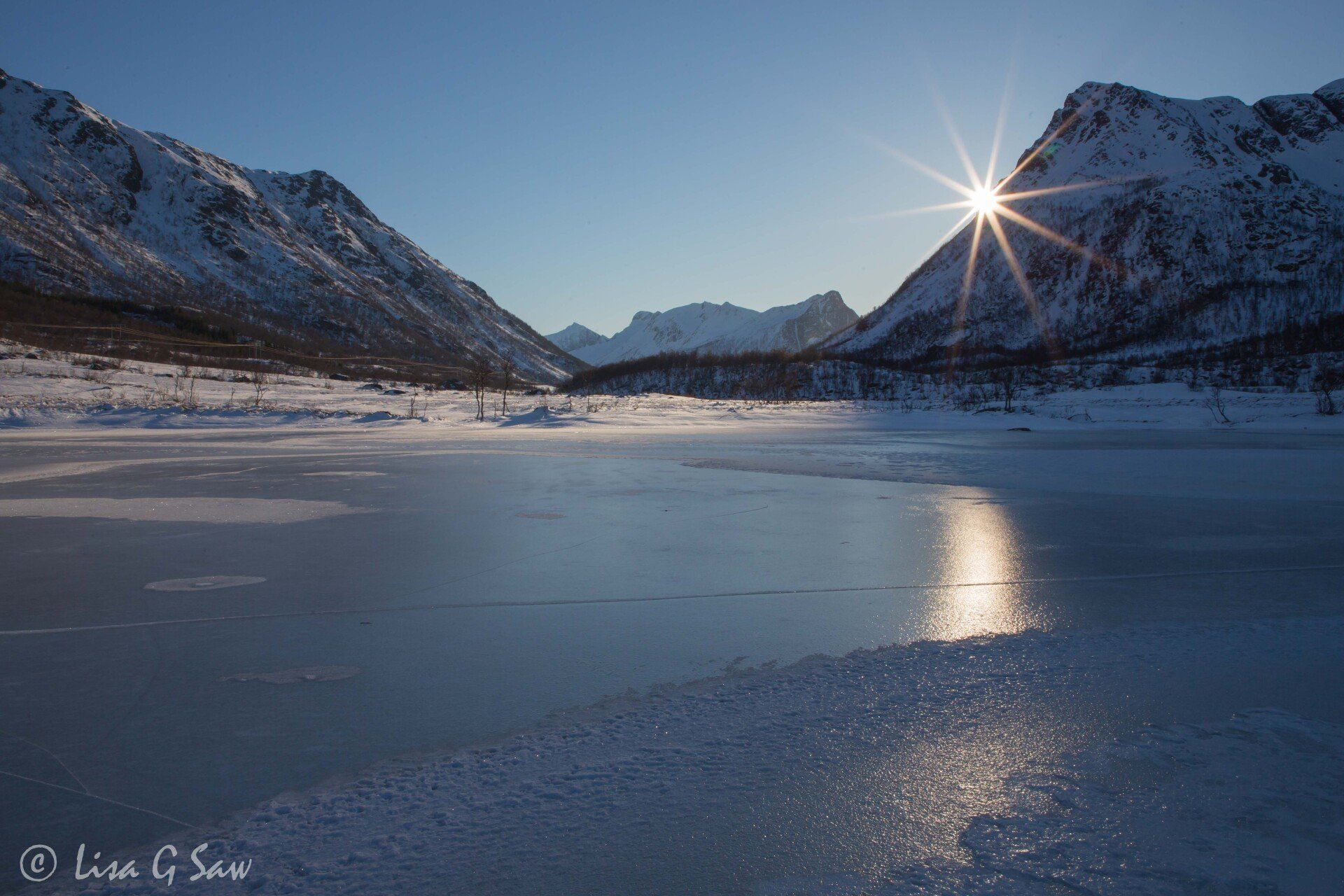 Frozen lake and sunburst behind mountain