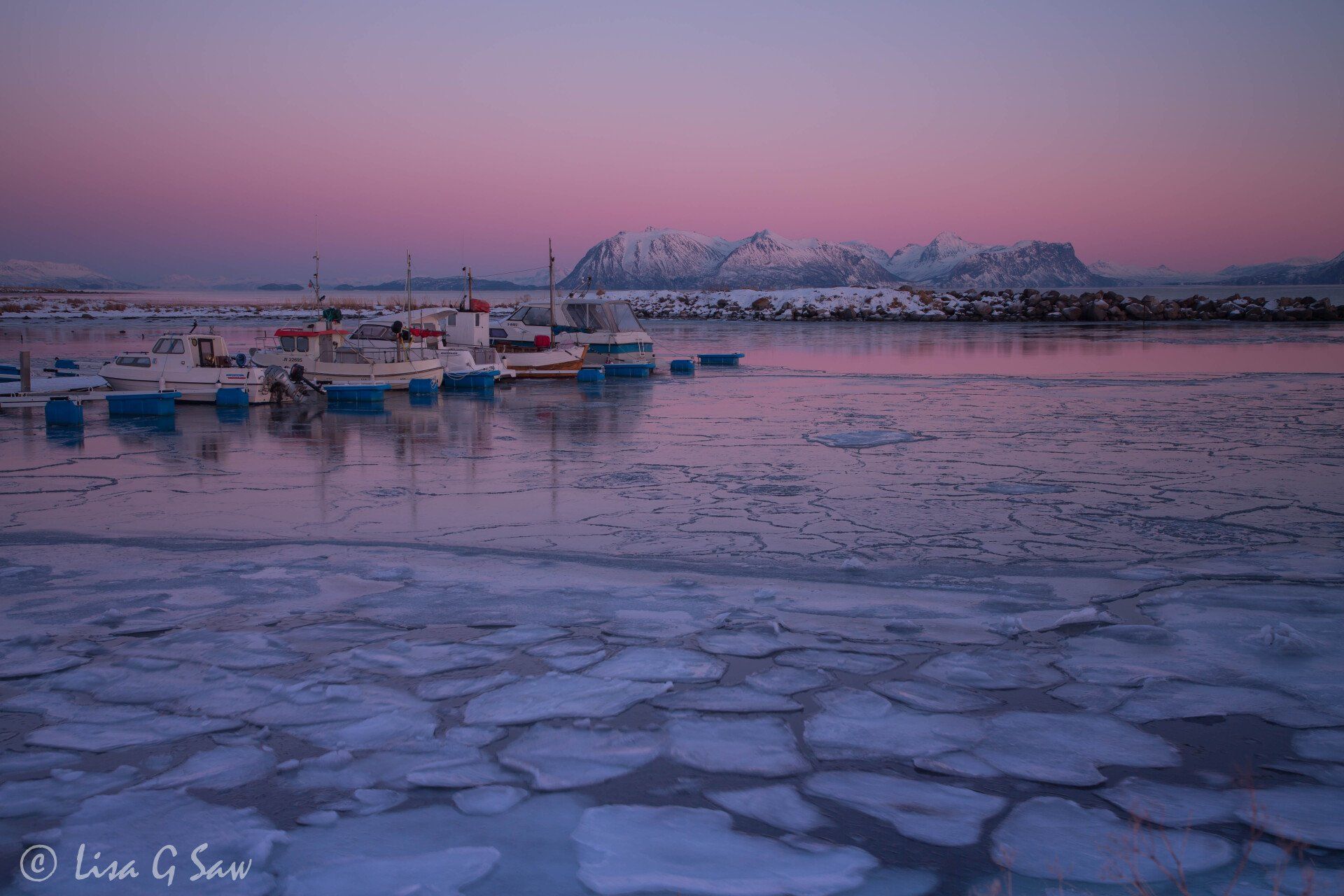 Boats by jetty and broken ice on water with mountains
