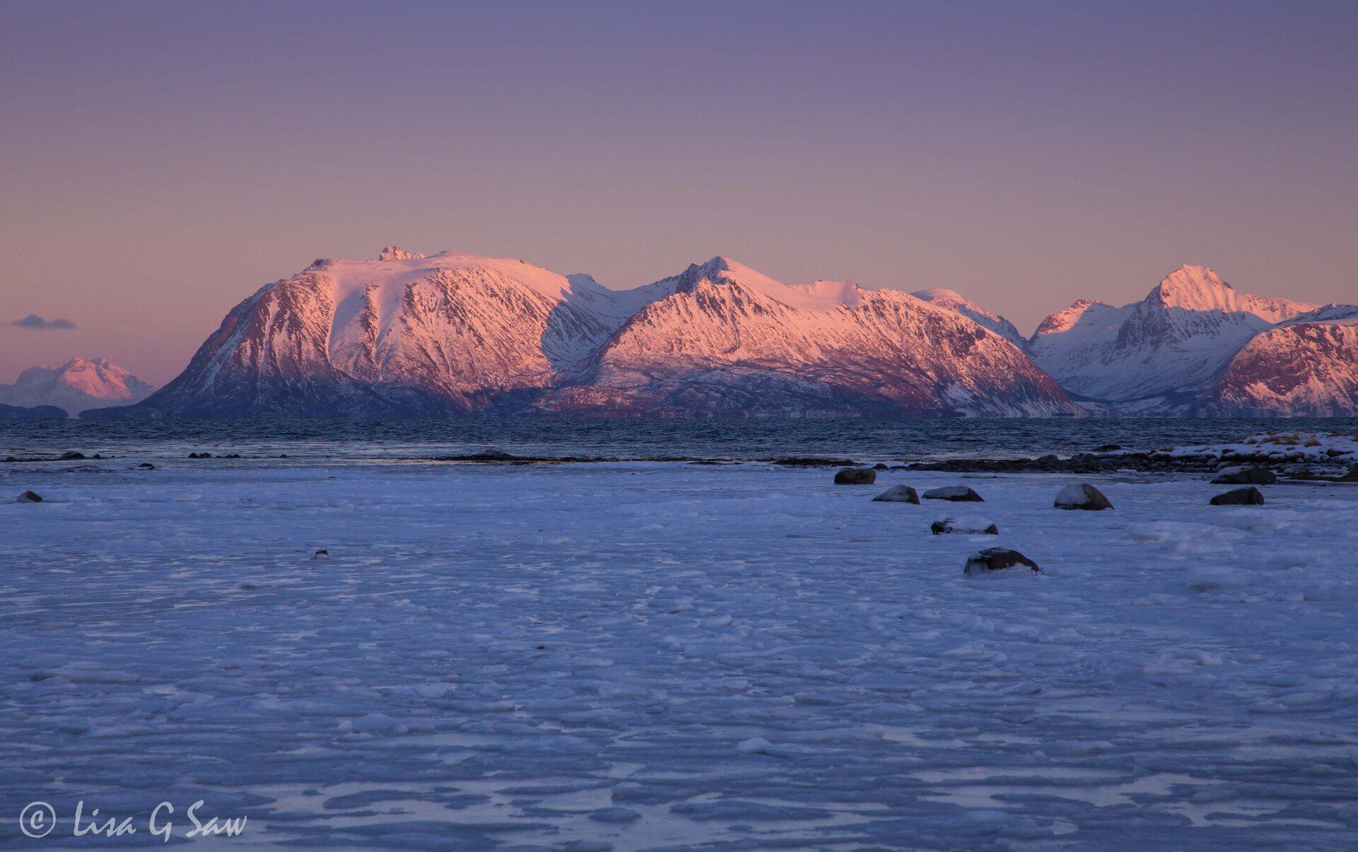 Stones in ice leading to snow covered mountains at sunset