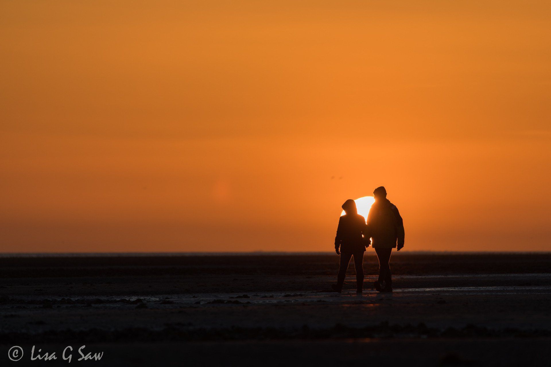 Couple walking on beach at sunset, sun behind them