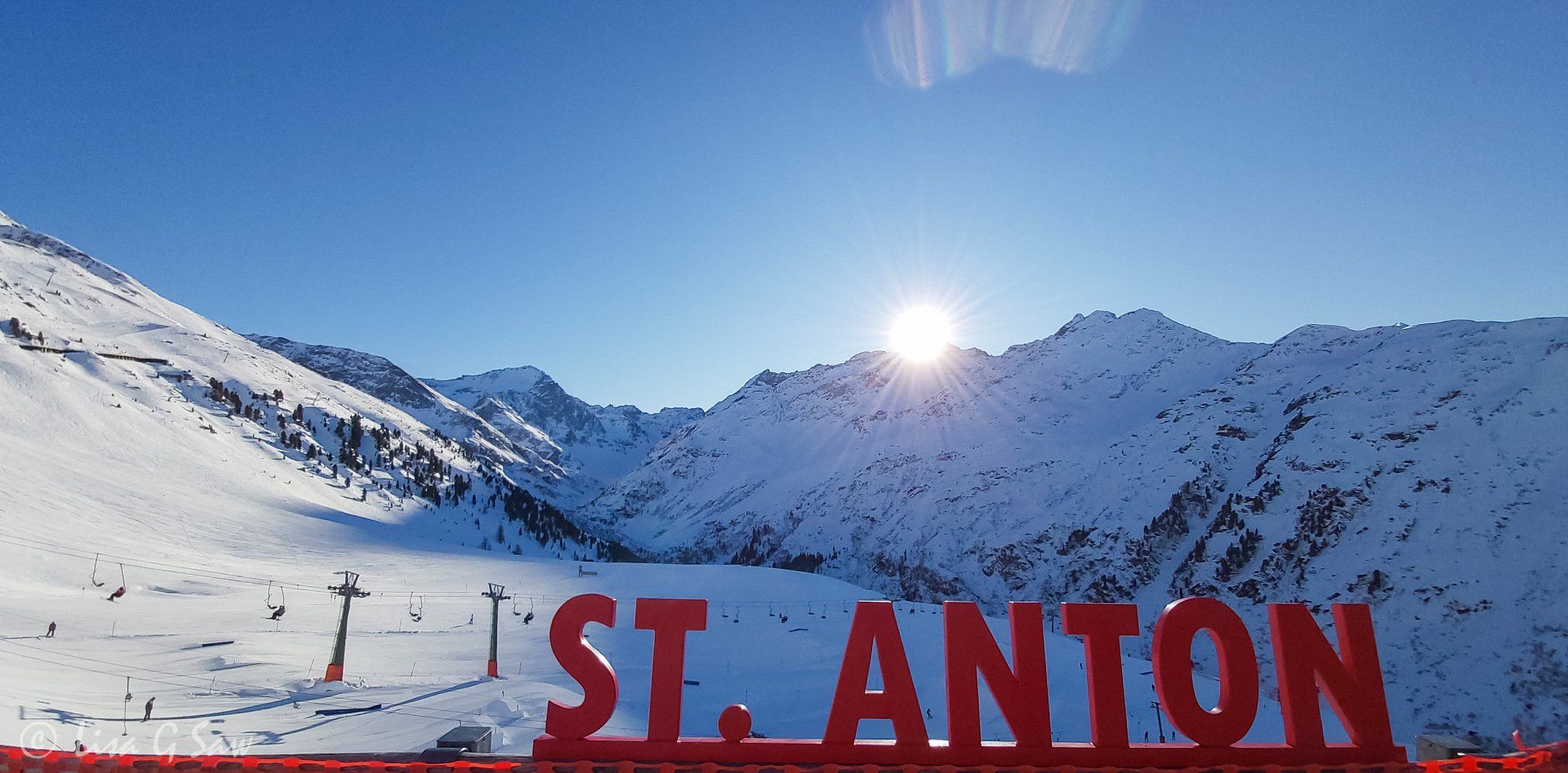 Sunburst behind snow capped mountains with St Anton sign