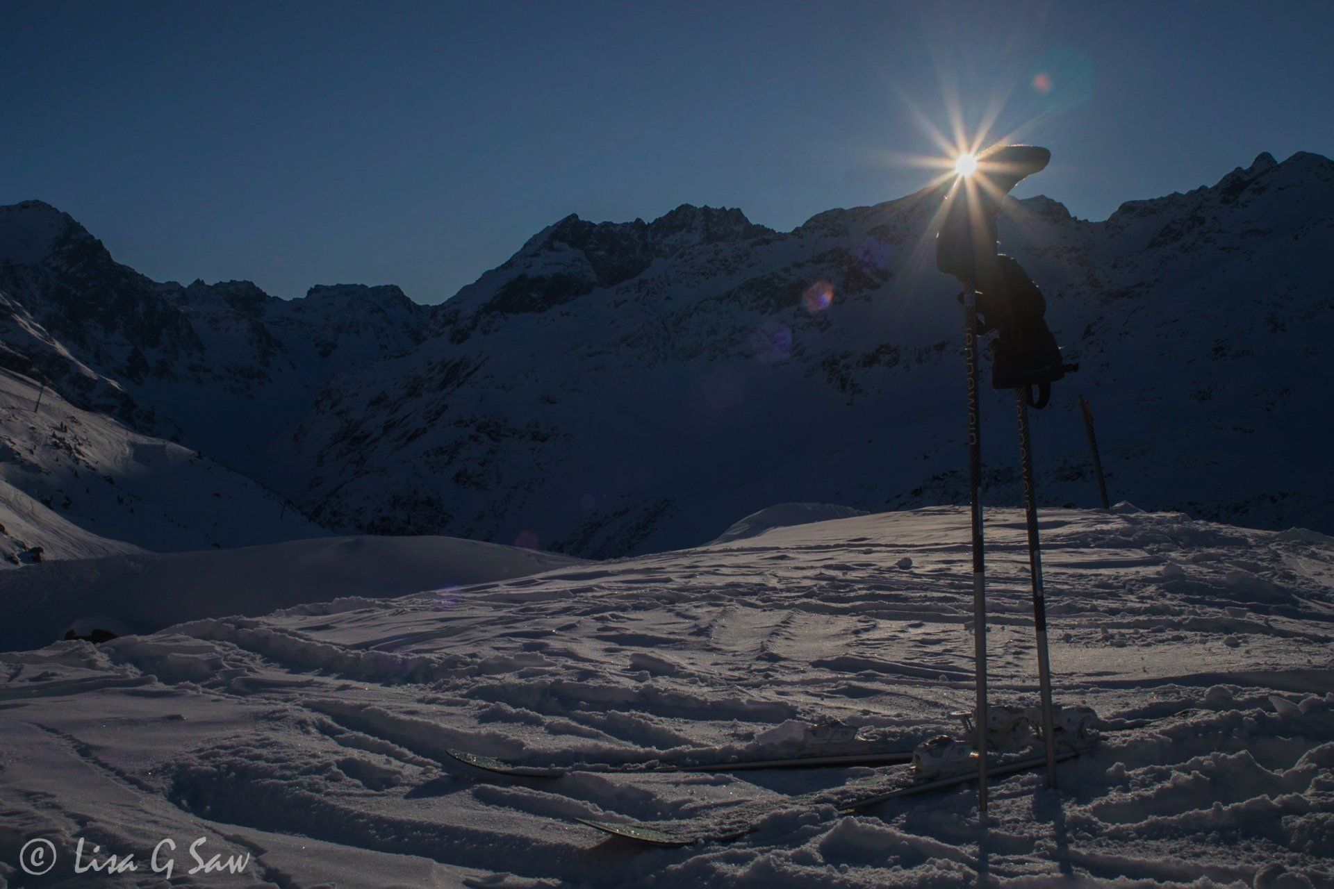 Sunburst behind mittens on ski poles with skis in snow