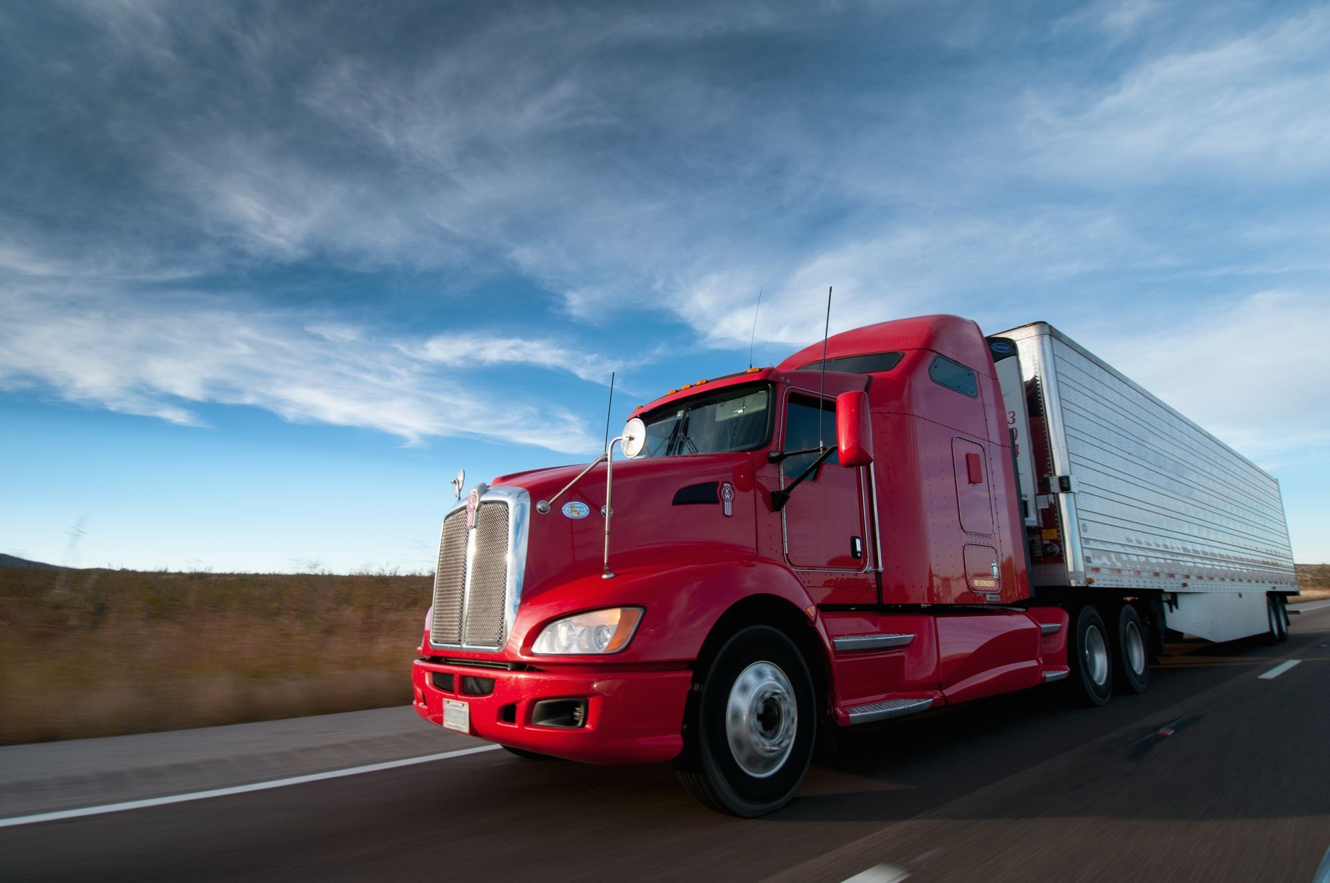 A red semi truck with a white trailer is driving down a highway.