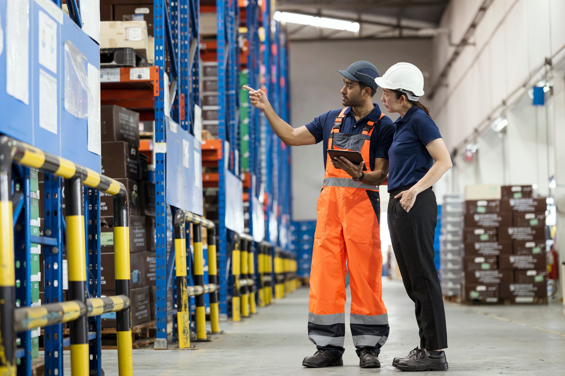 A man and a woman are standing in a warehouse looking at a tablet.
