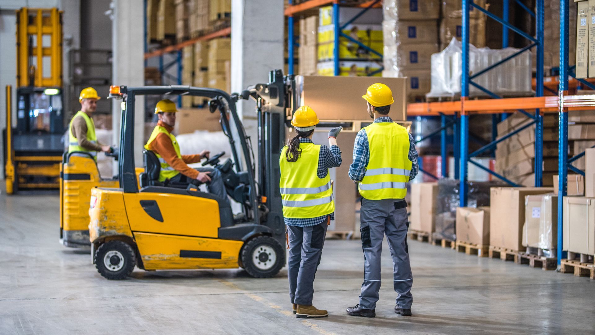 A group of workers are standing in front of a forklift in a warehouse.