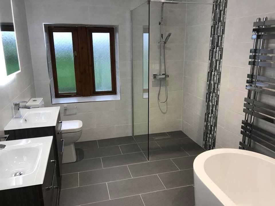 Modern bathroom with gray tile floor, glass shower, dual sinks, and a white bathtub.