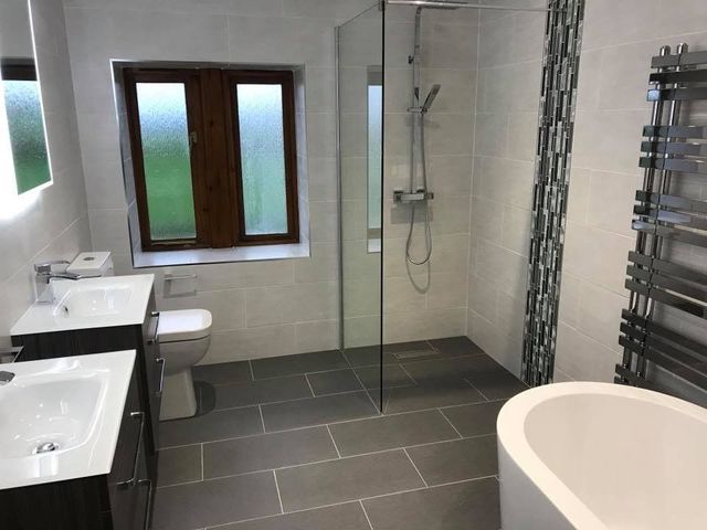 Modern bathroom with gray tile floor, glass shower, dual sinks, and a white bathtub.
