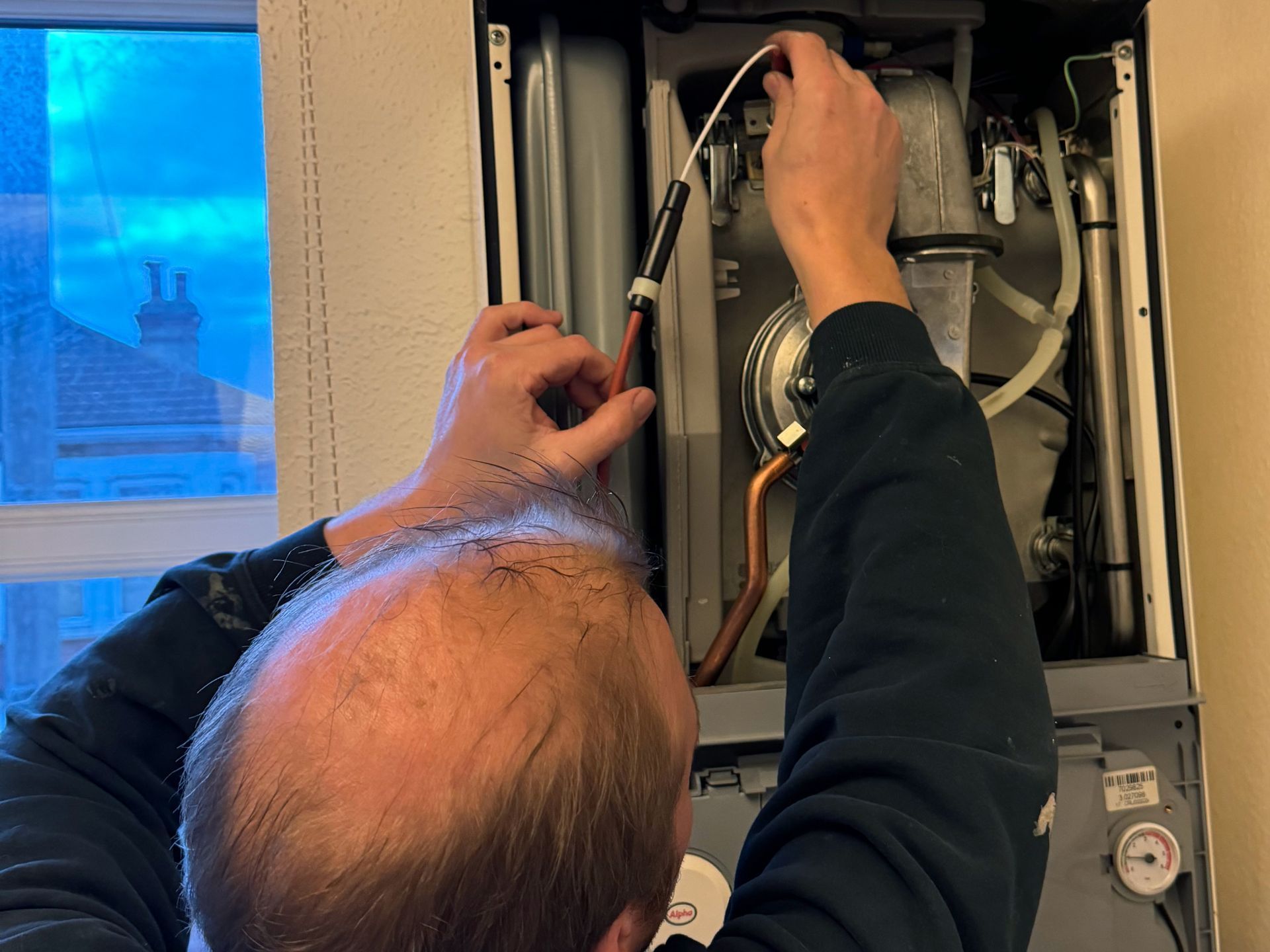 Person working on a boiler, inserting a part. Interior setting.
