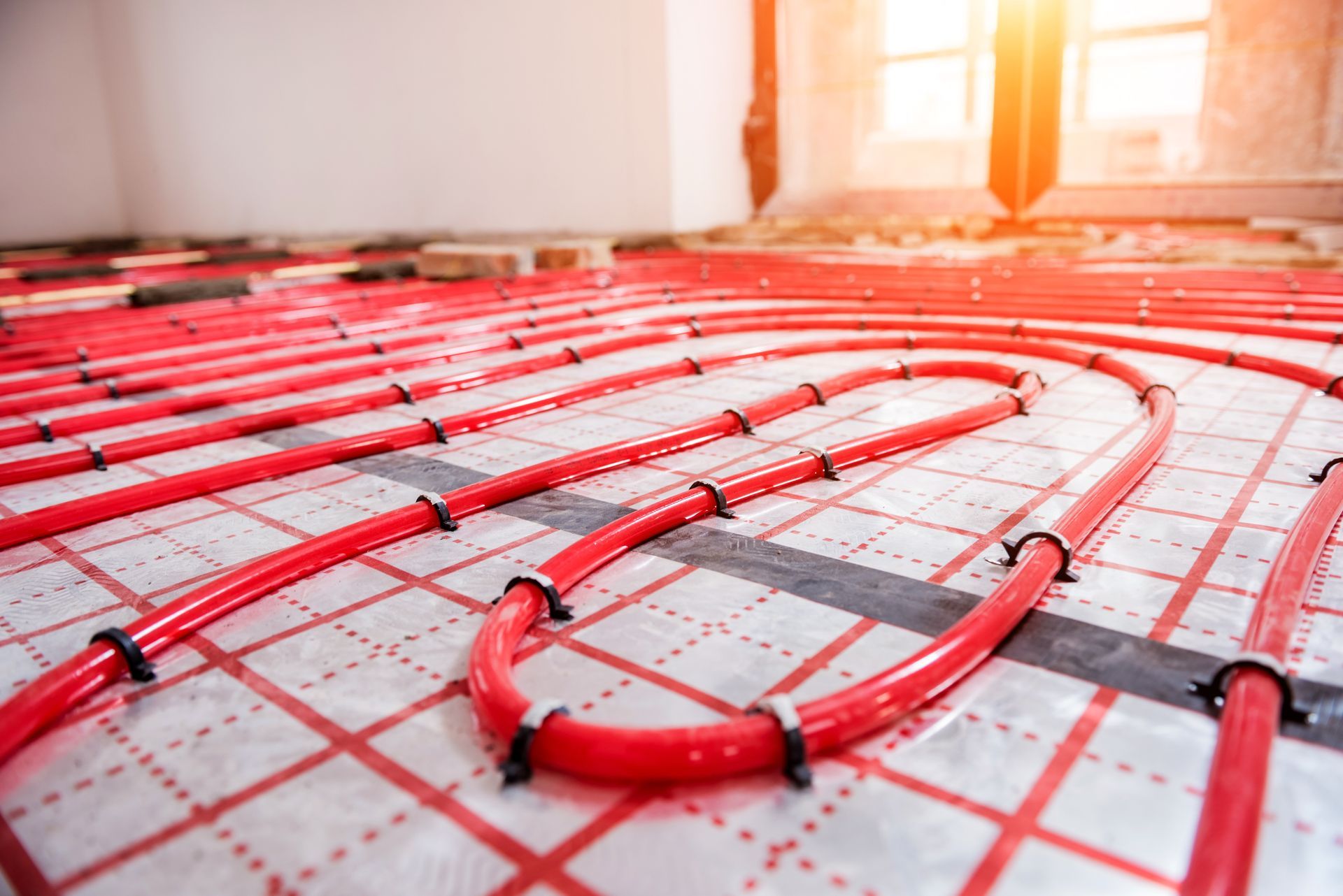 Red radiant floor heating tubes installed on a grid, ready for concrete.