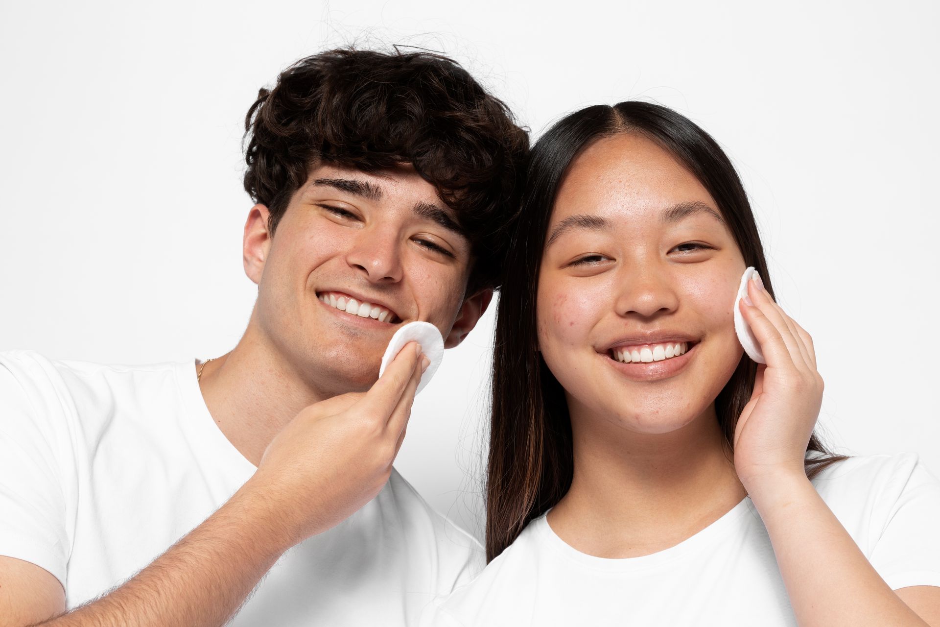 A man and a woman are cleaning their faces with cotton pads.