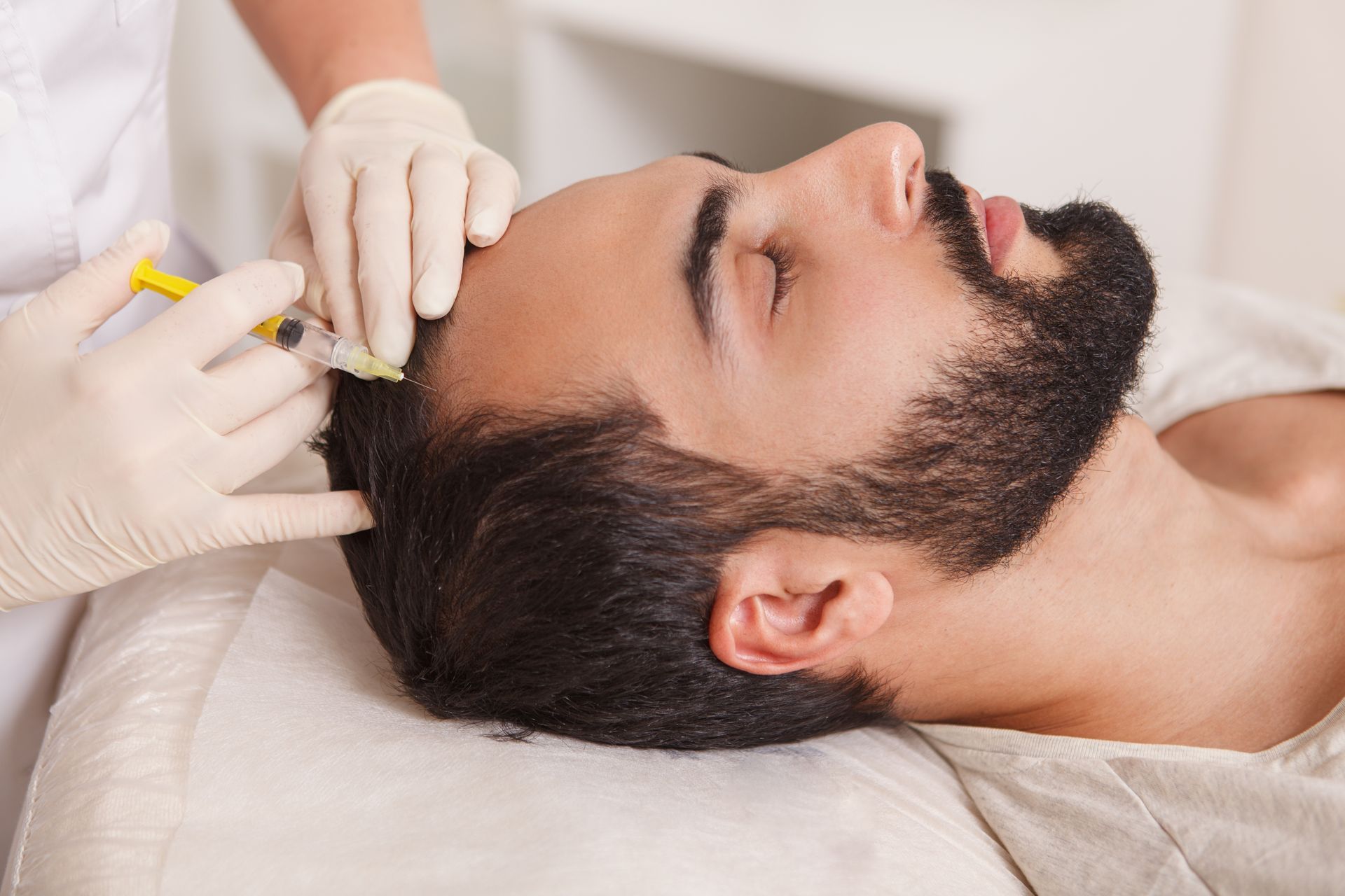 Man receiving hair treatment injections on his scalp, by a gloved person with a syringe.