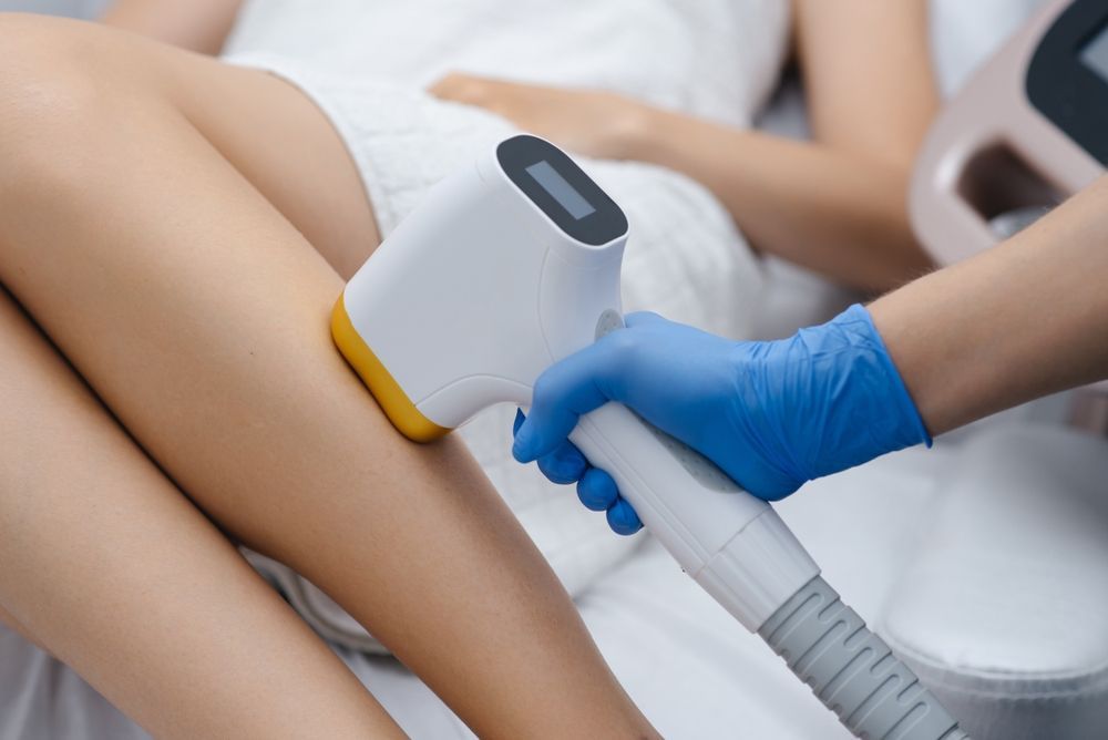 Laser hair removal treatment on a leg, blue-gloved hand holding device, white background.