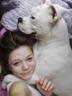 White Boxer dog hugging young girl