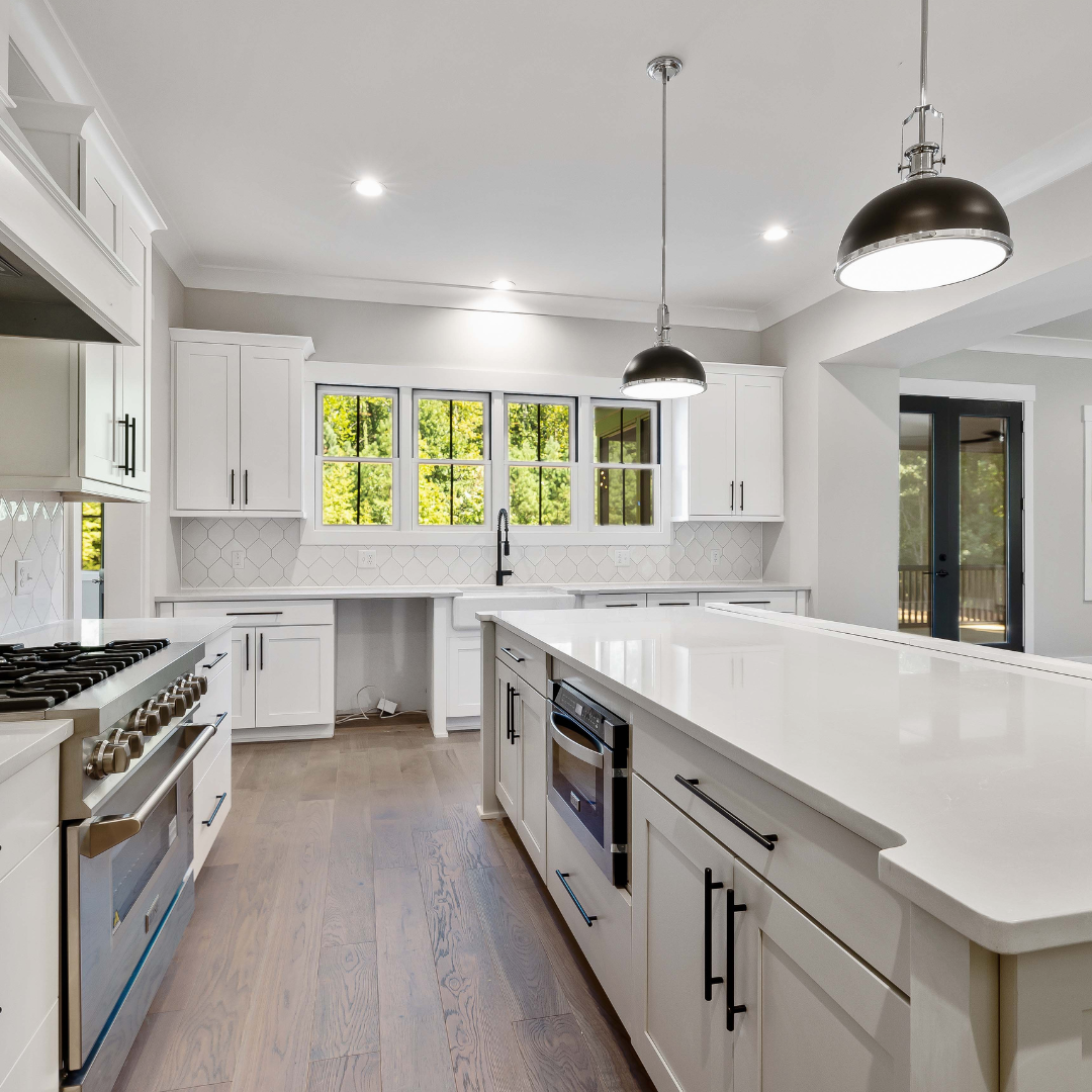 Modern white kitchen with a large island, stainless steel appliances, and wooden floors.