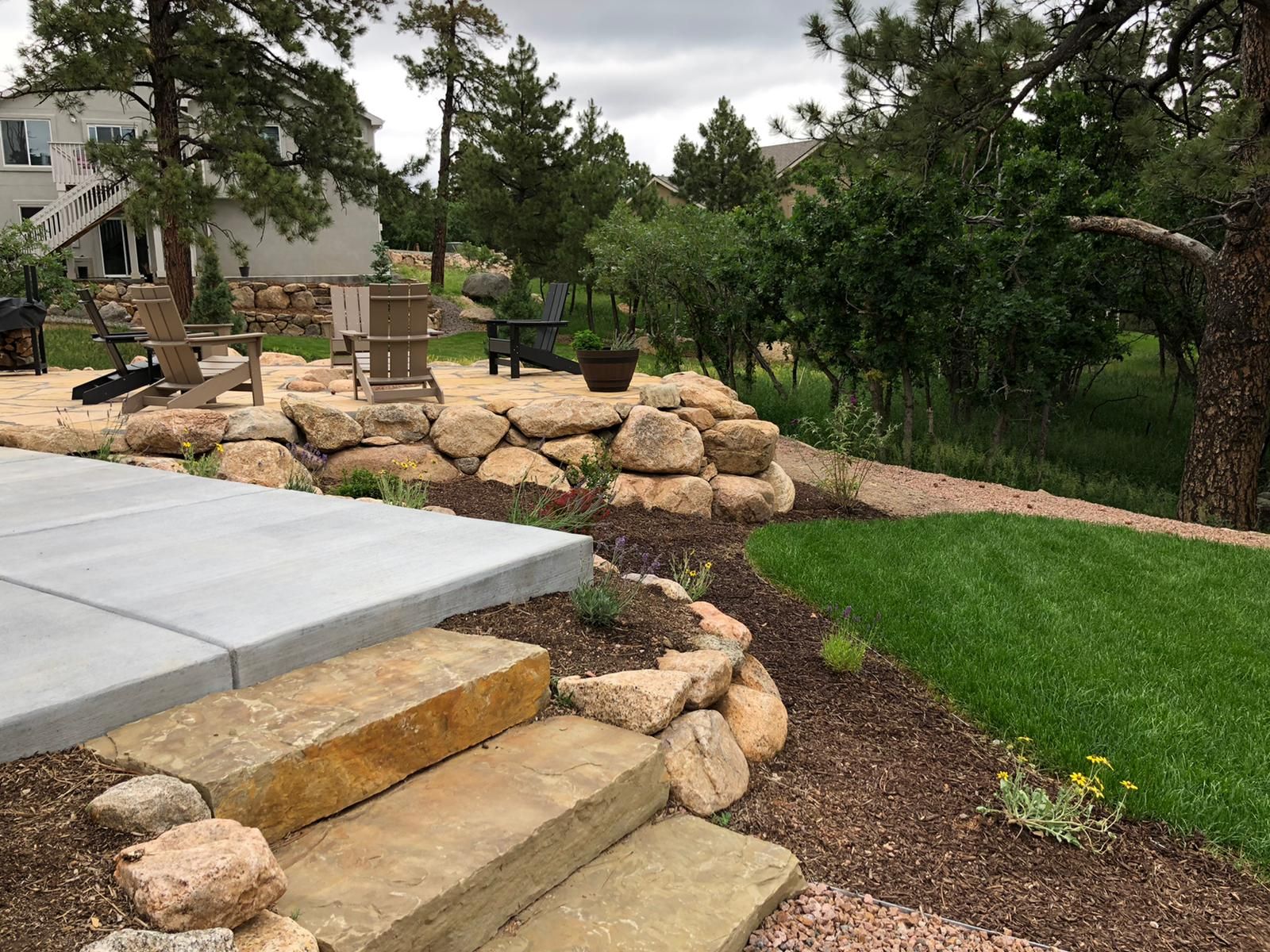 A stone staircase leading up to a patio with chairs and trees in the background.