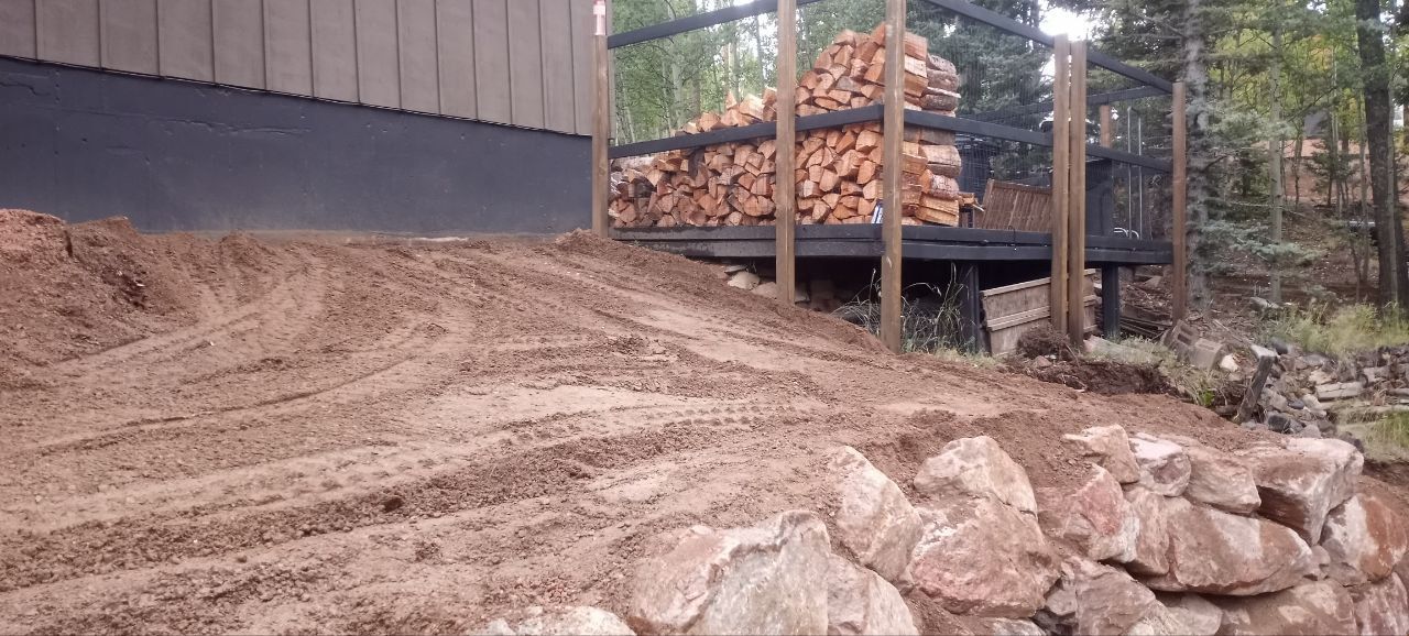 A pile of wood is sitting on top of a dirt hill in front of a house.