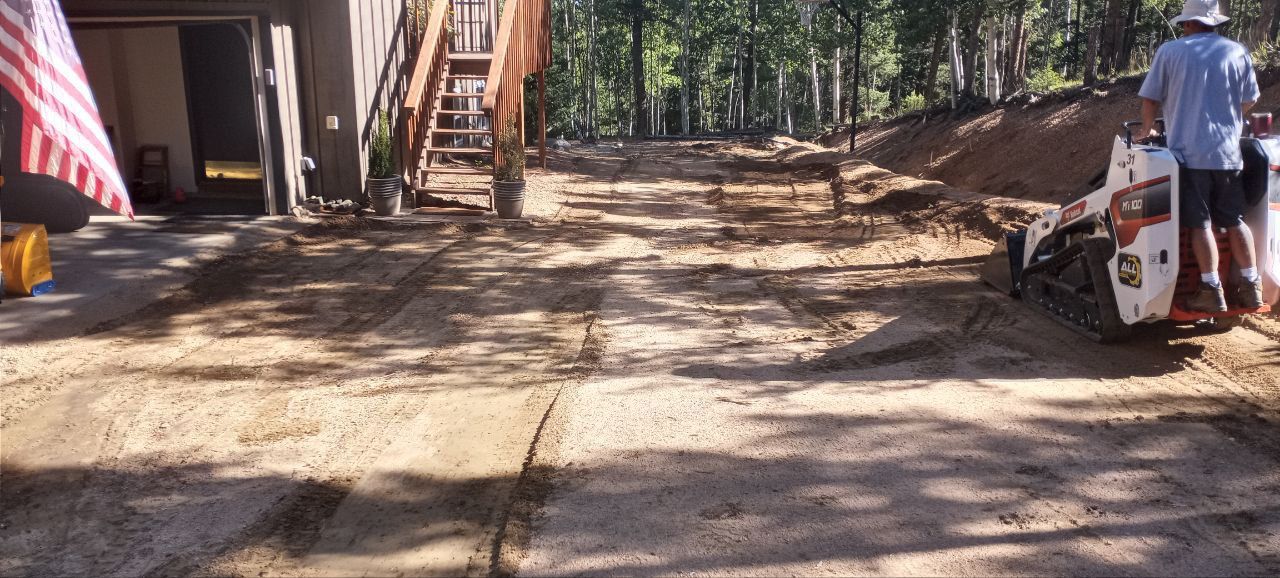 A man is driving a bobcat tractor down a dirt road