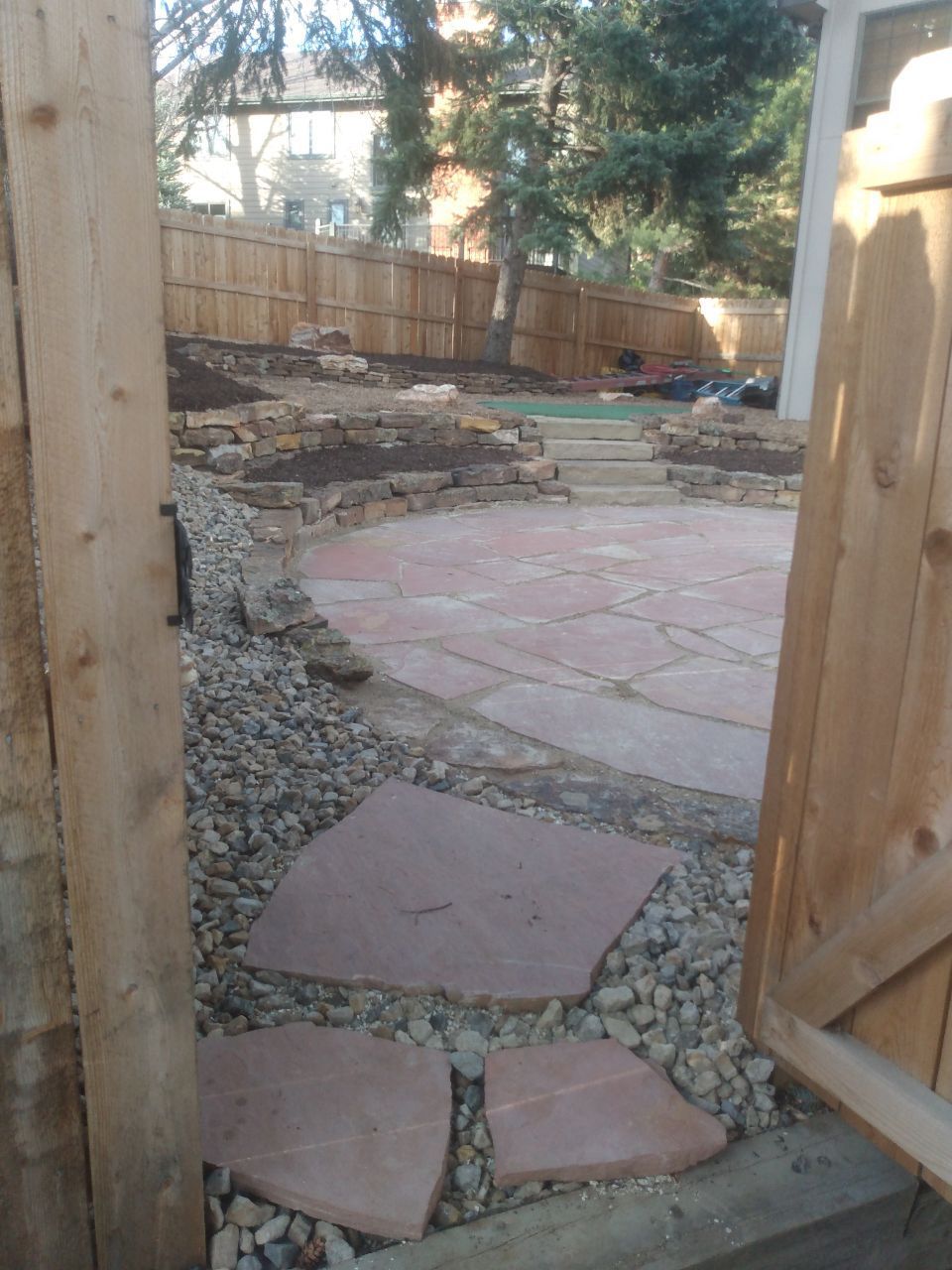 A wooden fence is open to a stone walkway