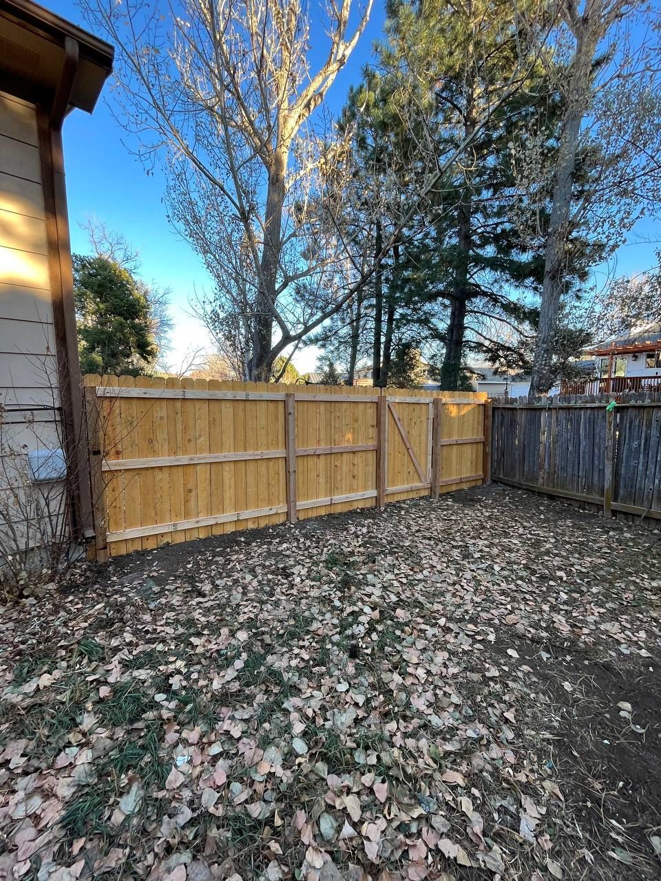 A wooden fence is in the backyard of a house surrounded by trees.