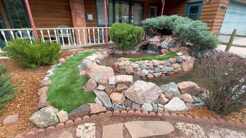 A garden with a waterfall in front of a log cabin.