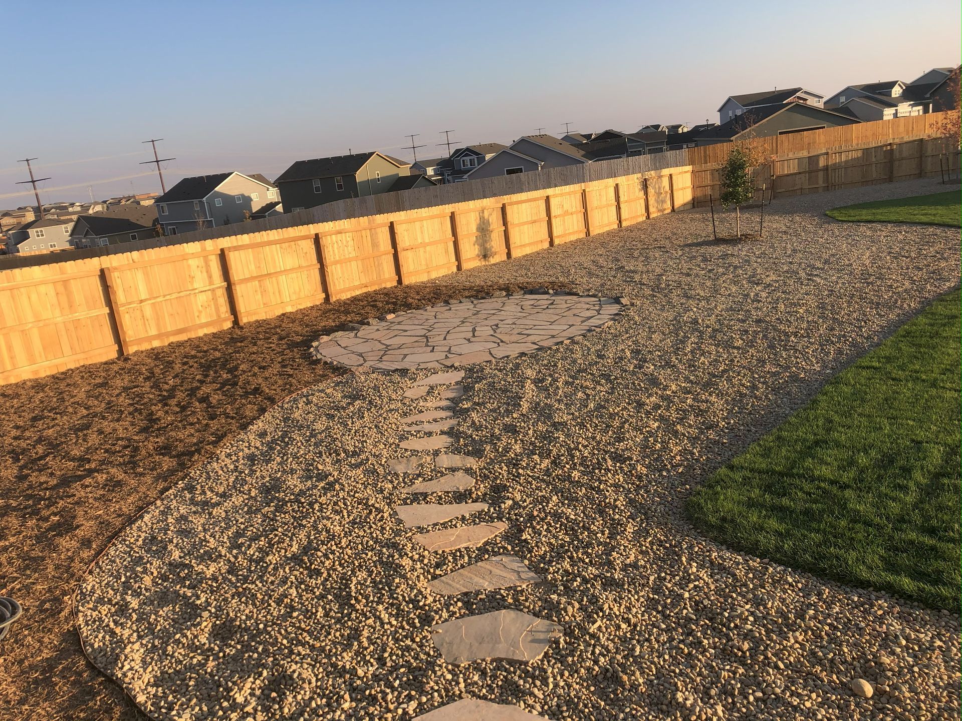 A gravel path leading to a wooden fence with houses in the background