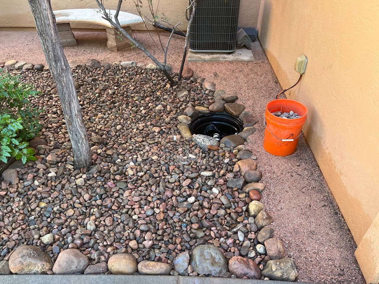 A bucket of rocks is sitting next to a hole in the ground.