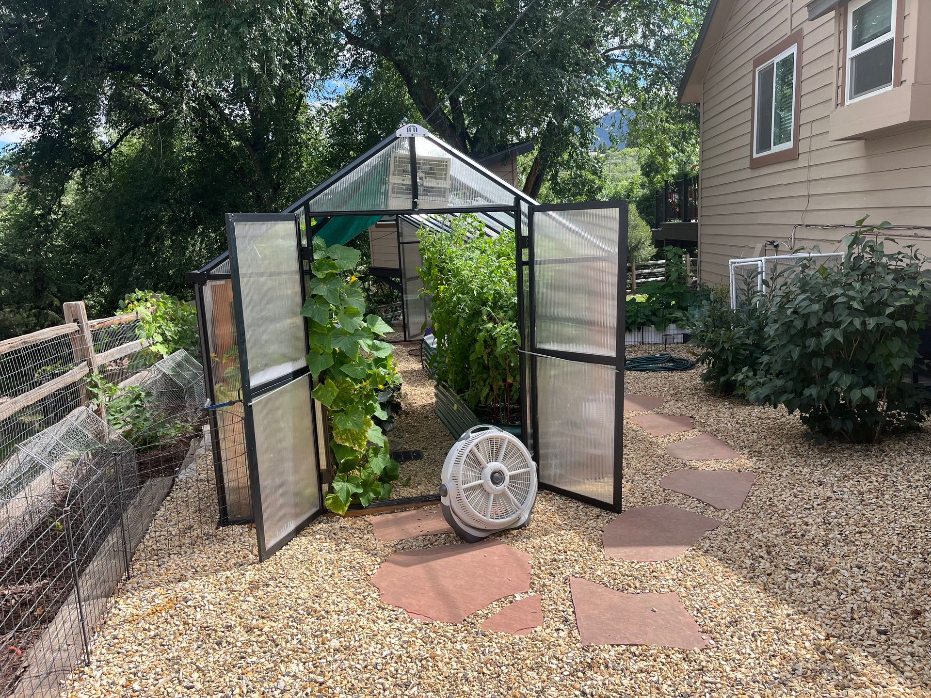 A greenhouse in a backyard with a fan in front of it