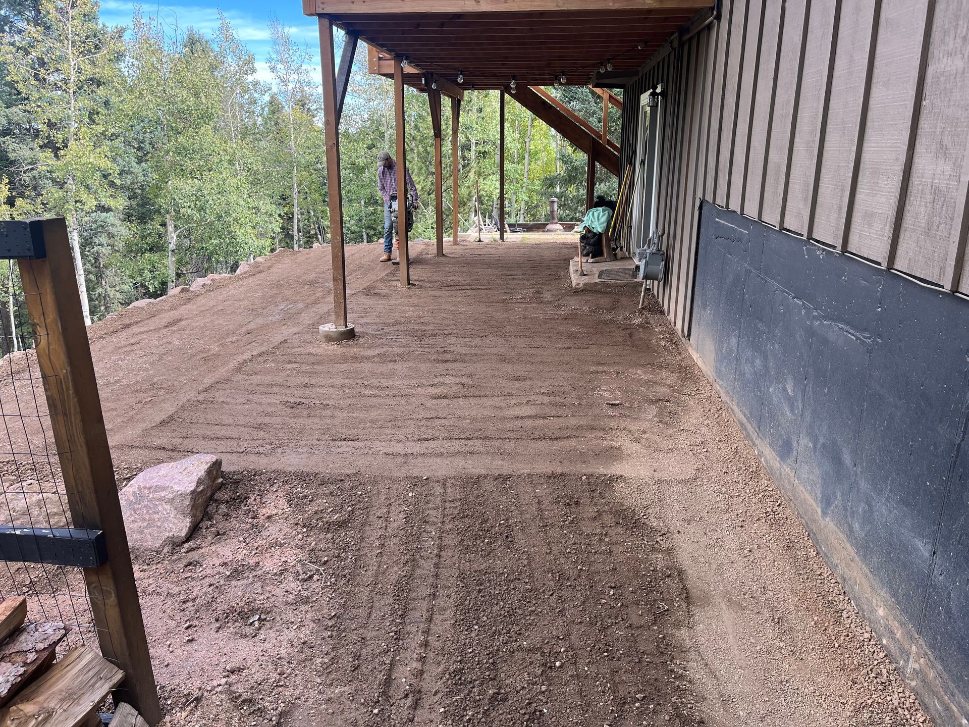 A man is standing on a dirt path next to a house.