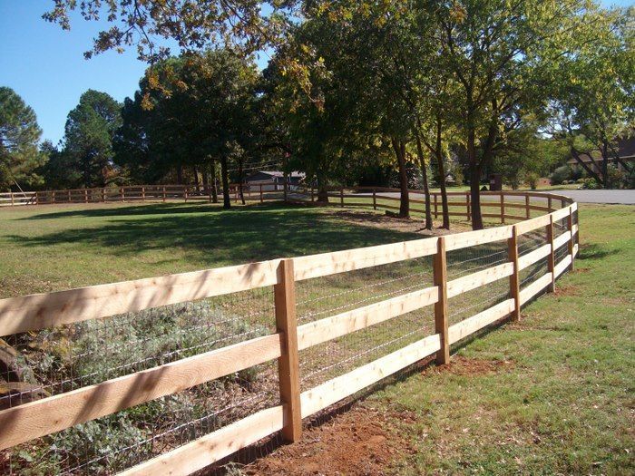 A wooden fence surrounds a grassy field with trees in the background
