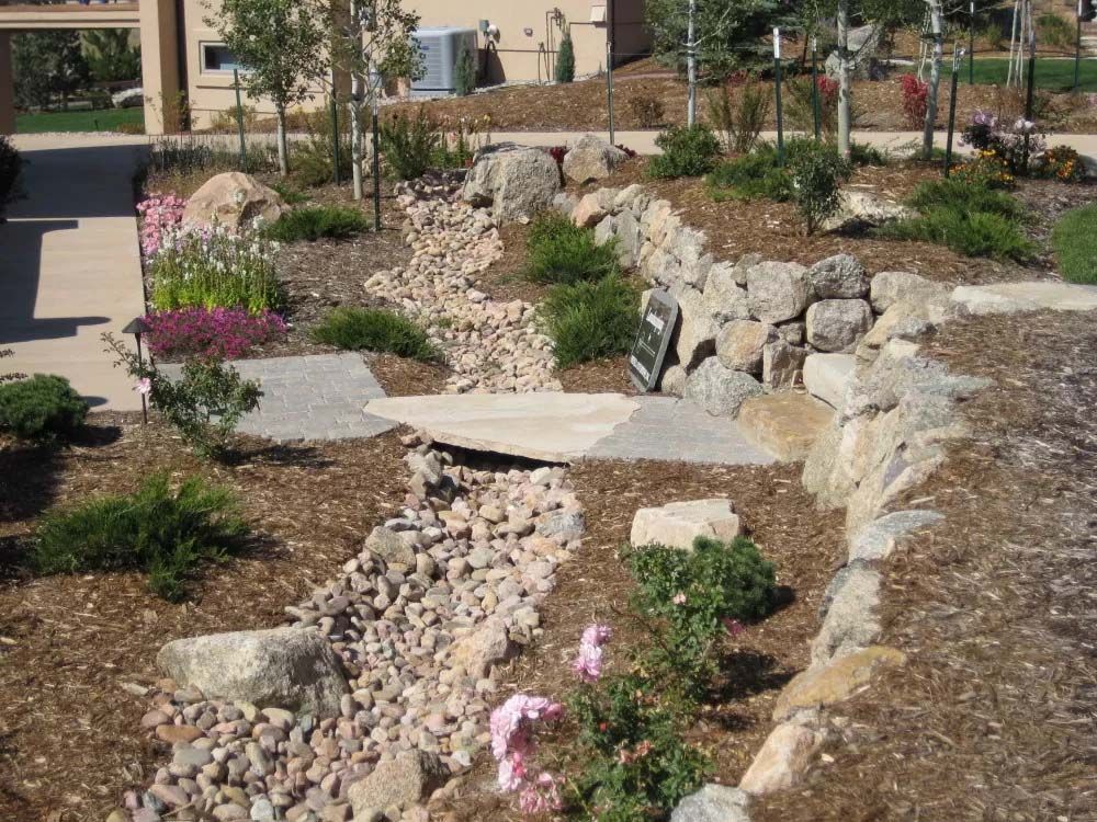 Landscaped rock garden with dry creek bed and small stone bridge.