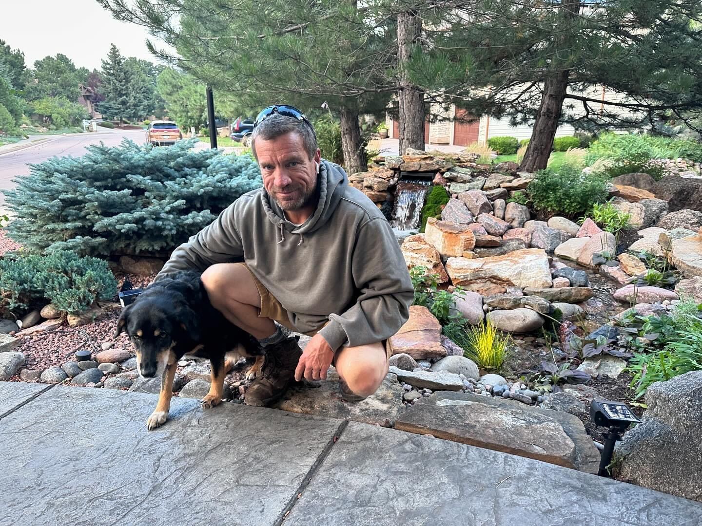 A man is kneeling down next to a dog on a sidewalk.