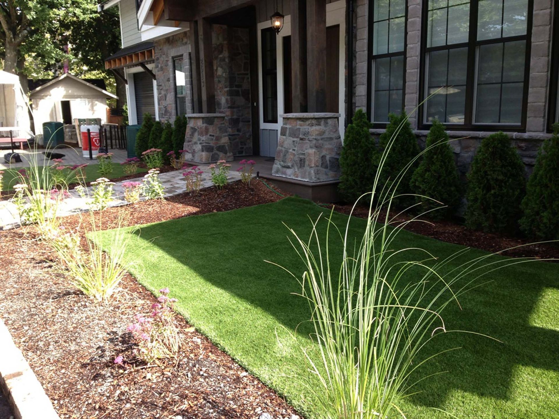 Front yard with a manicured lawn, shrubs, and ornamental grass near a stone-faced house.