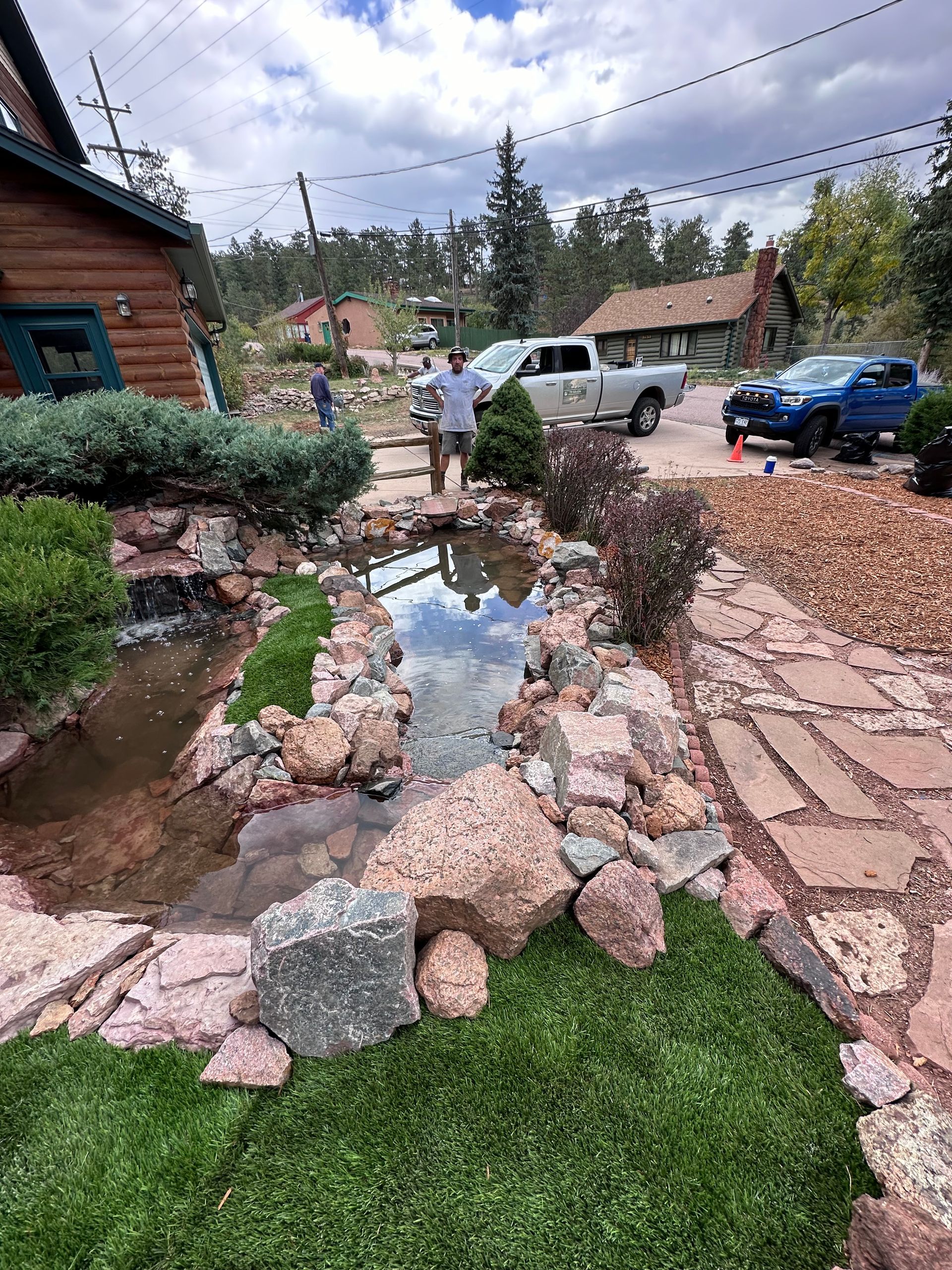 A man is standing in front of a pond in a yard.