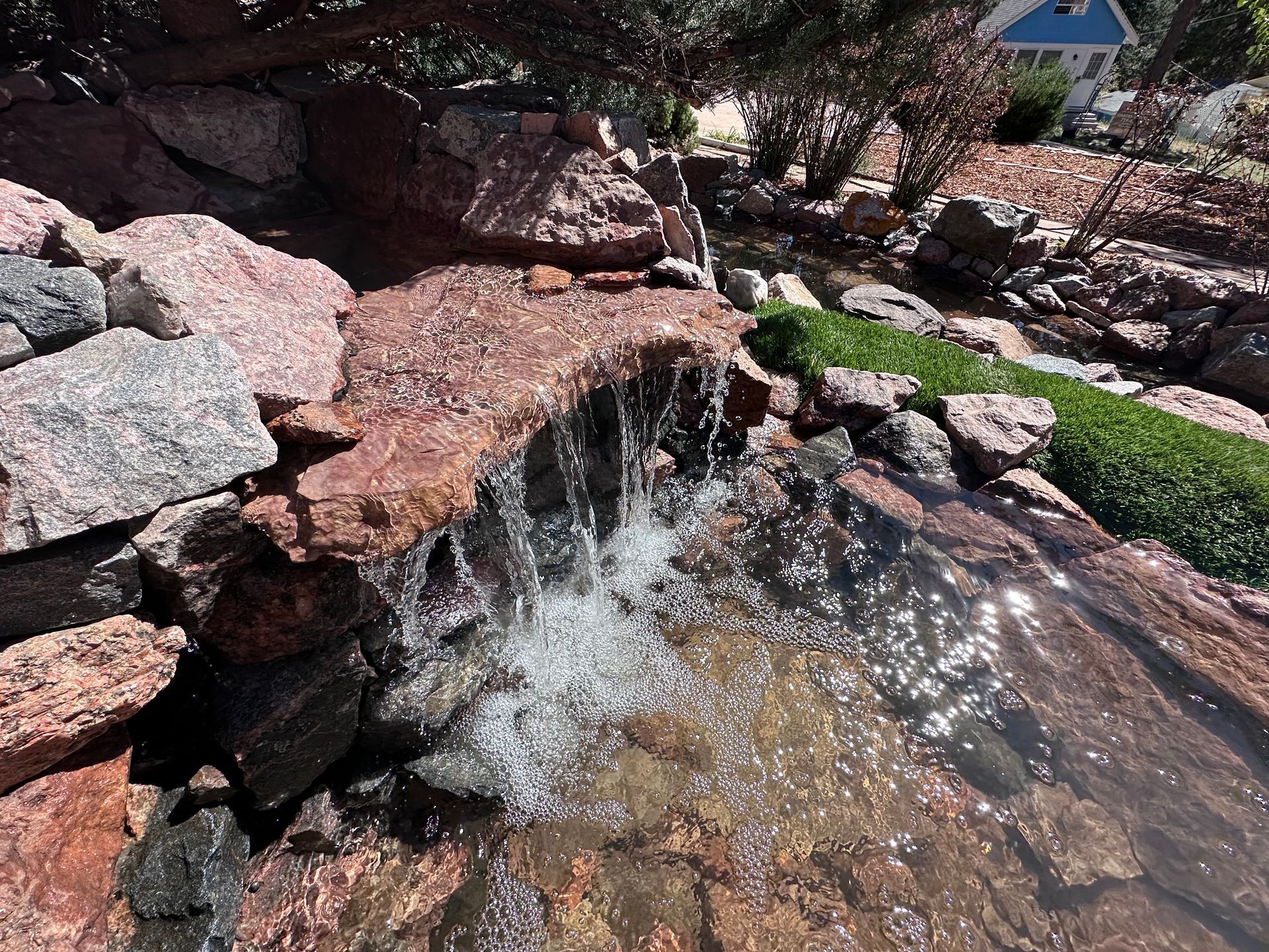A small waterfall in a rocky area with a house in the background