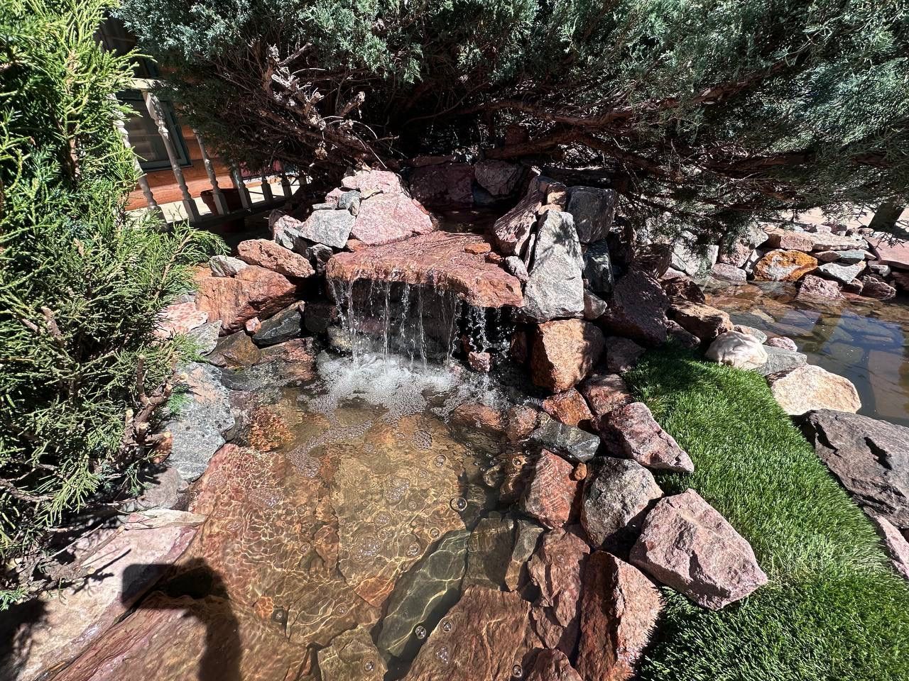 A small waterfall is surrounded by rocks and trees in a garden.
