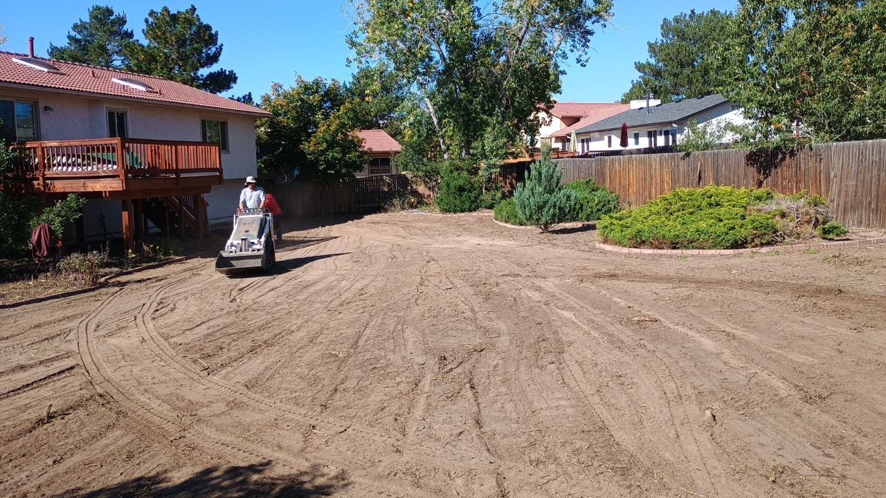 A man is driving a bulldozer on a dirt road in front of a house