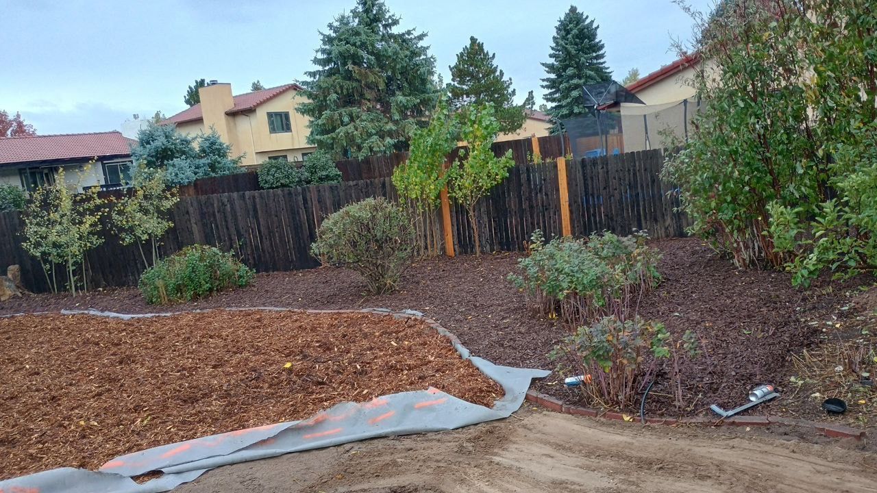 A backyard with a fence and a pile of mulch