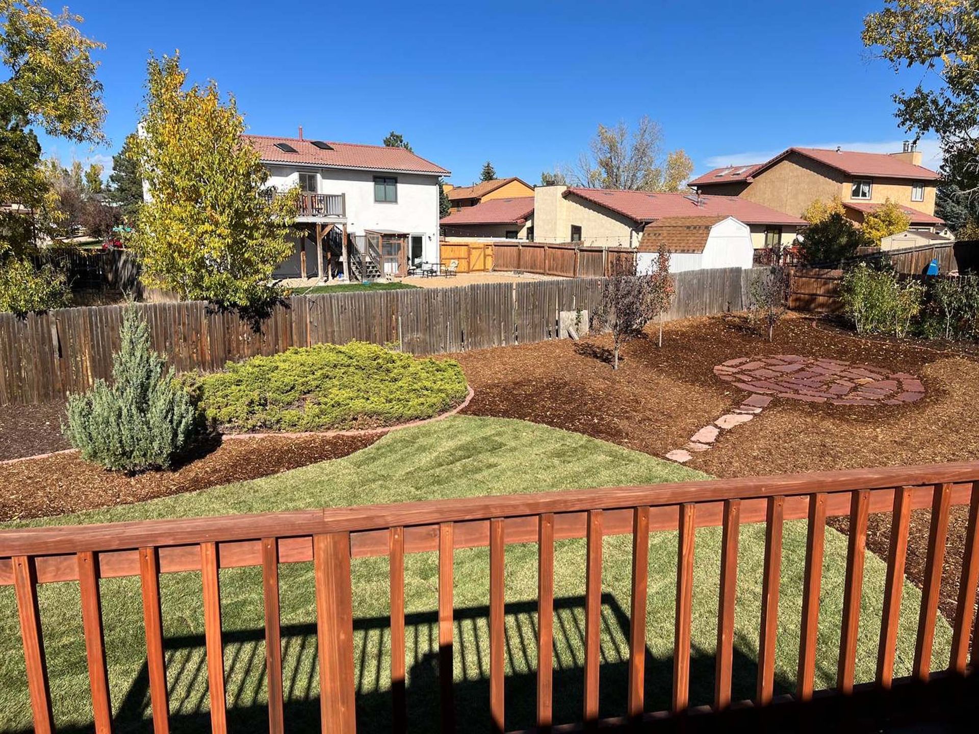 Backyard view with a wooden deck, lawn, mulch, and houses.