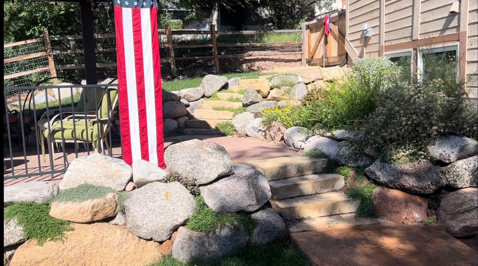 An american flag is hanging from a pole in a backyard.