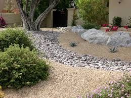 Landscaped front yard with gravel, rocks, bushes, and a tree, creating a natural desert-like appearance.
