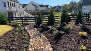 A landscaped yard with a dry creek bed and dark fence, surrounded by homes under a blue sky.