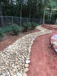 Stone path winding through dirt and greenery, near a fence and trees.