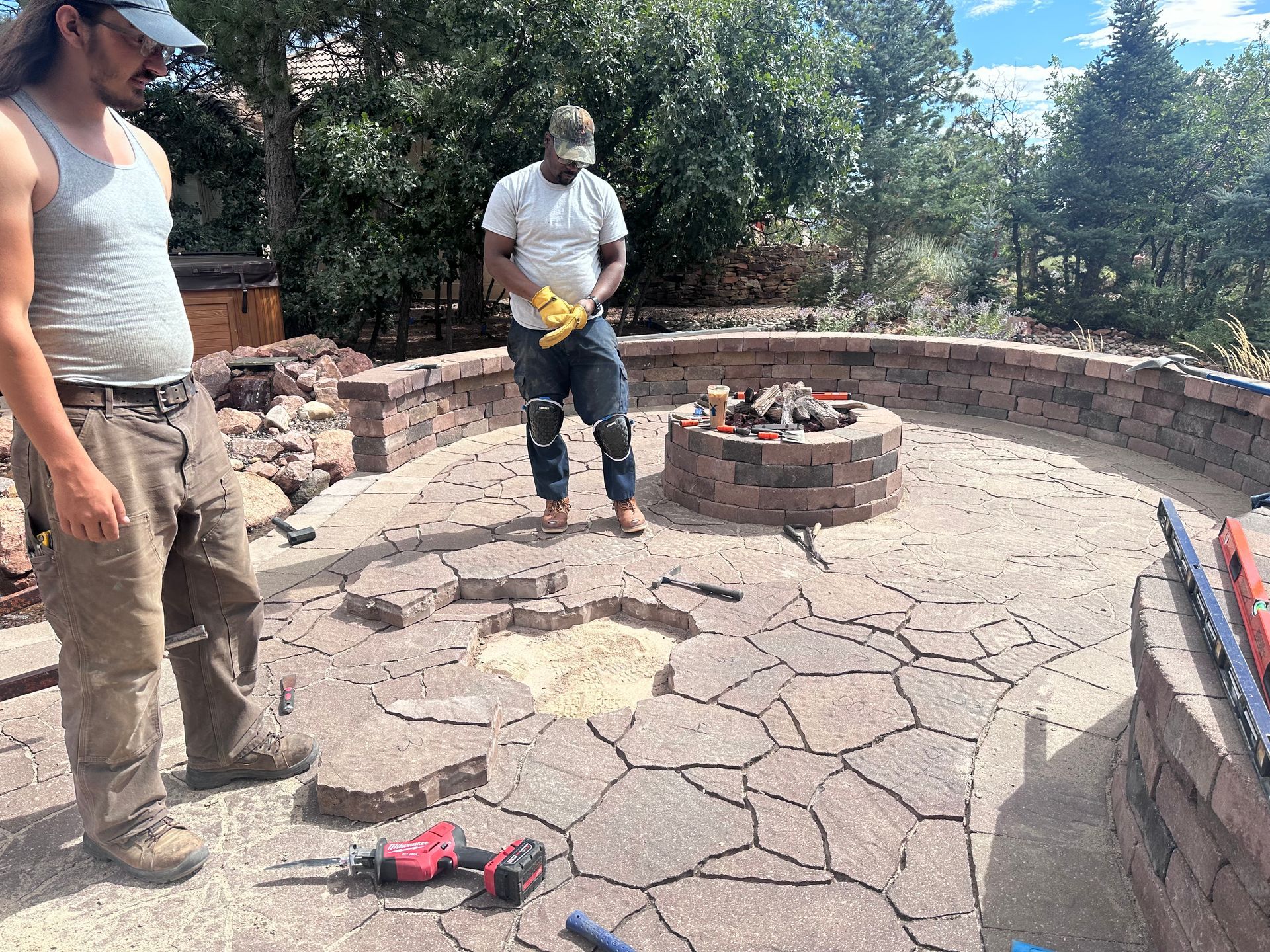 Two men are working on a fire pit in a backyard