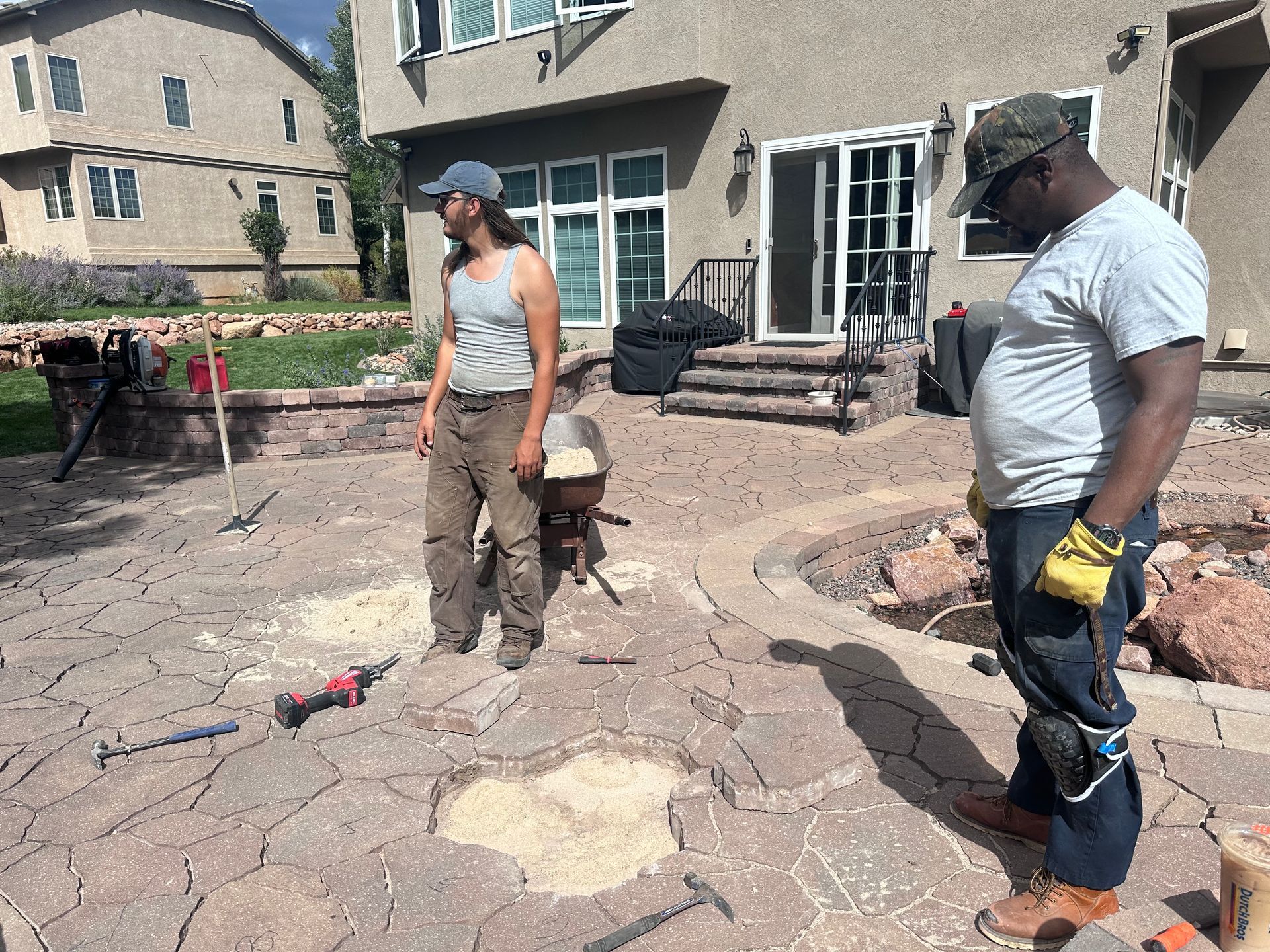 Two men are working on a patio in front of a house