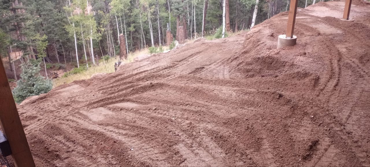 A large pile of dirt on a hillside with trees in the background.