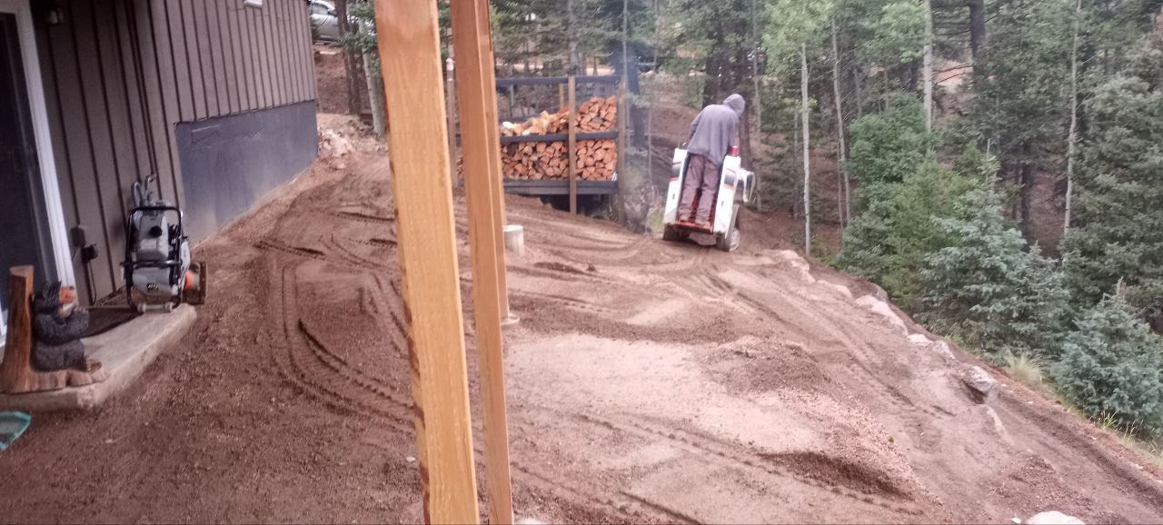 A man is riding a bulldozer on a dirt road next to a house.