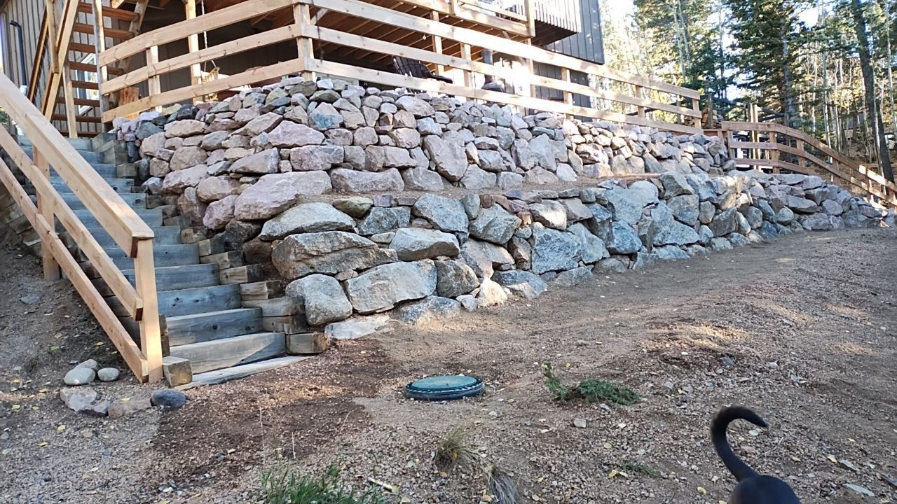 A black cat is standing in front of a stone wall and stairs